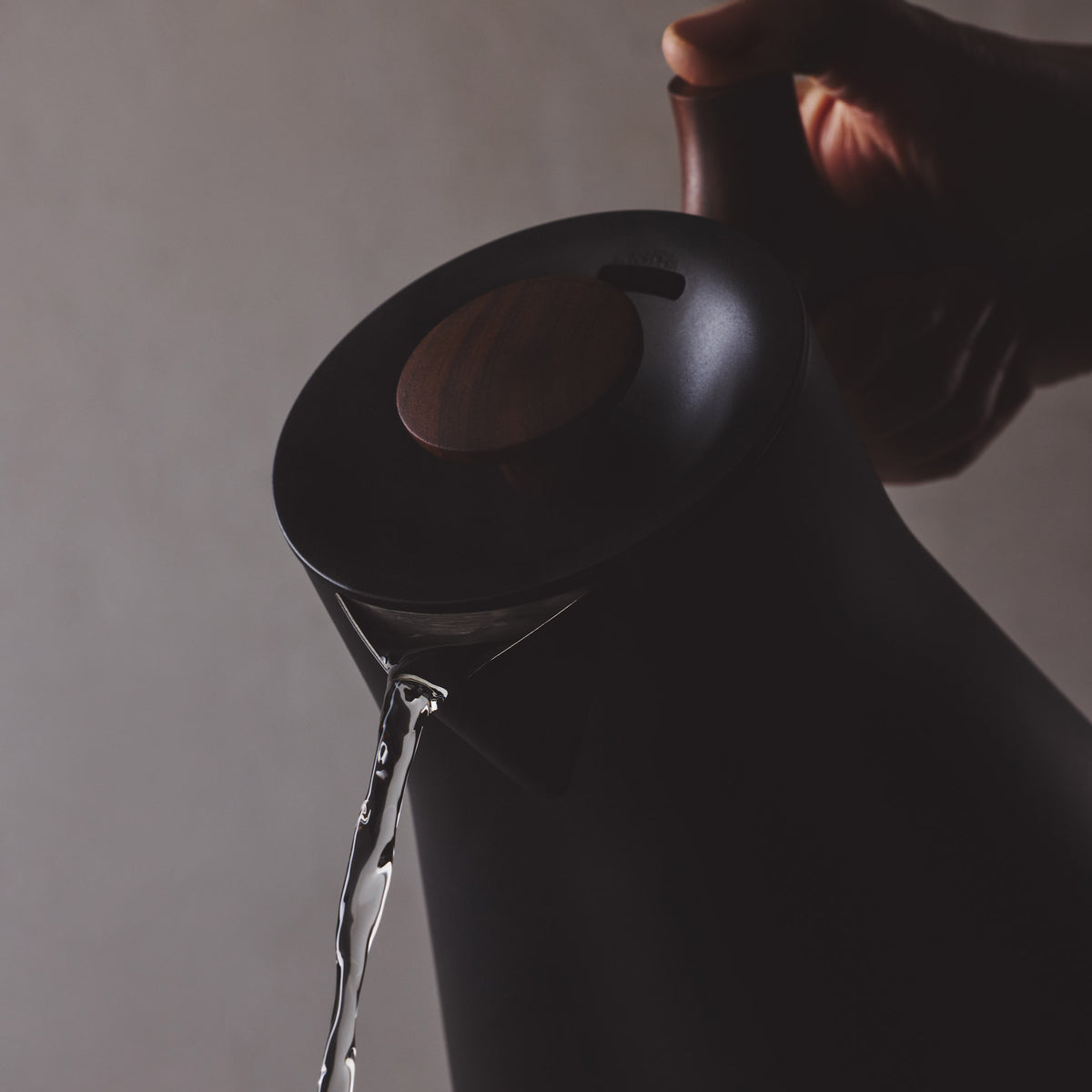 Schwarzer Wasserkocher mit Holzgriff, Wasser fließt ruhig in eine Tasse.