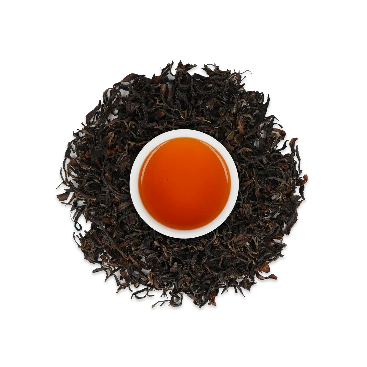 Weiße Keramiktasse mit leuchtend orange-braunem Schwarztee, umgeben von losen schwarzen Teeblättern.