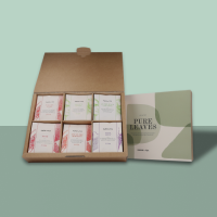 Offene Pappschachtel mit sechs pastellfarbenen Pure Leaves Tee-Packungen und grün-beigem Booklet.