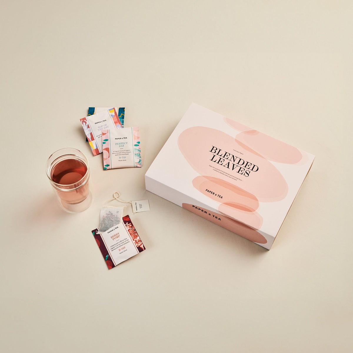 Pastellfarbene BLENDED LEAVES Teebox von PAPER & TEA mit buntem Tee und rosa Getränk.