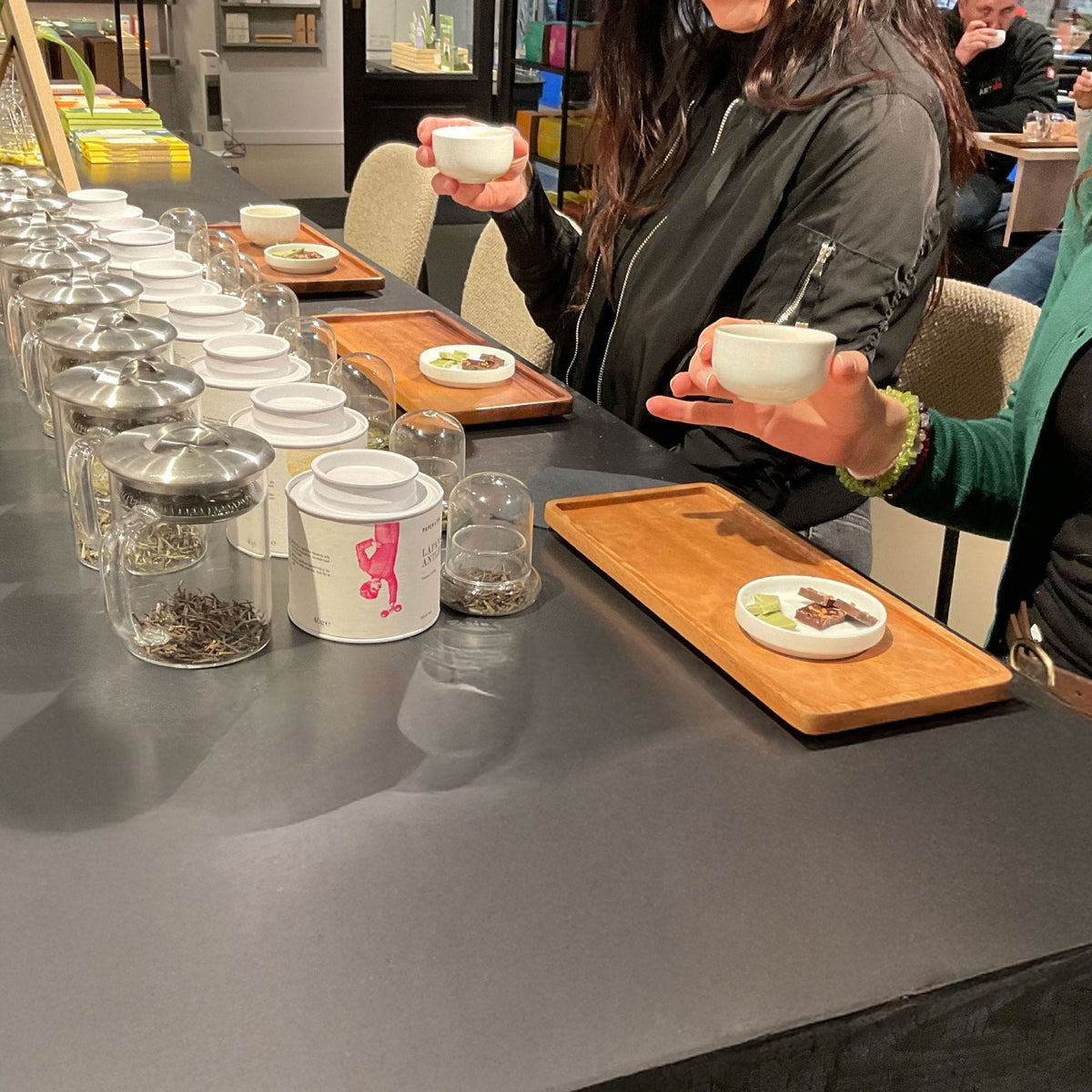 Zwei Frauen bei einer Teeverkostung mit weißen Tassen und Paper & Tea Produkten in einem gemütlichen Café.
