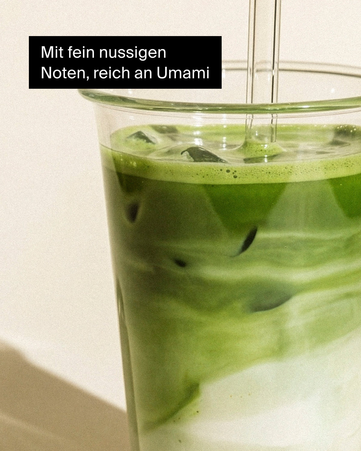 Hohes transparentes Glas mit Eistee aus Matcha, cremigem Milchwirl und Strohhalm, reich an Umami- und Nussnoten.