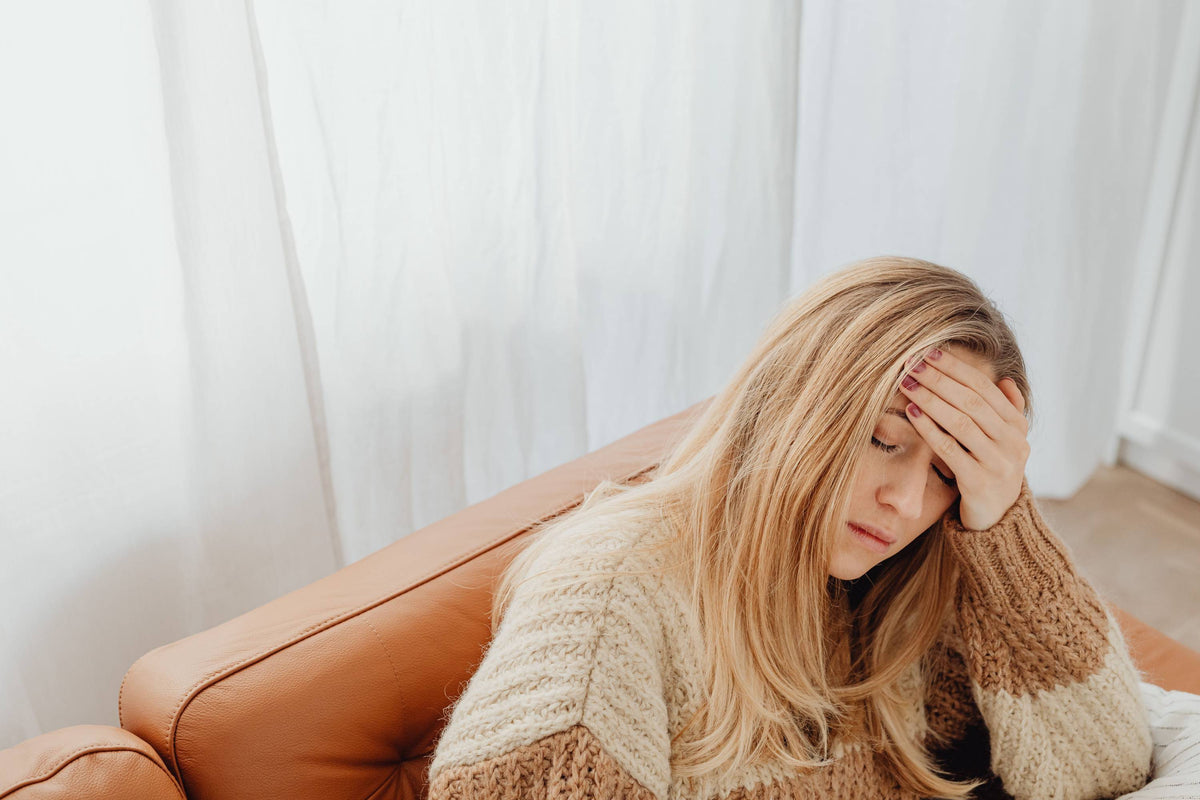 Junge blonde Frau im gestreiften Strickpullover auf Ledersofa hält sich die Hand an den Kopf