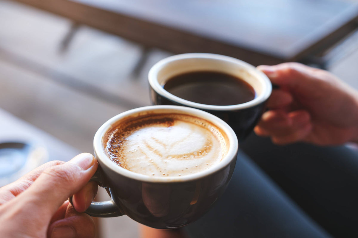 Zwei Personen stoßen mit Kaffeetassen an