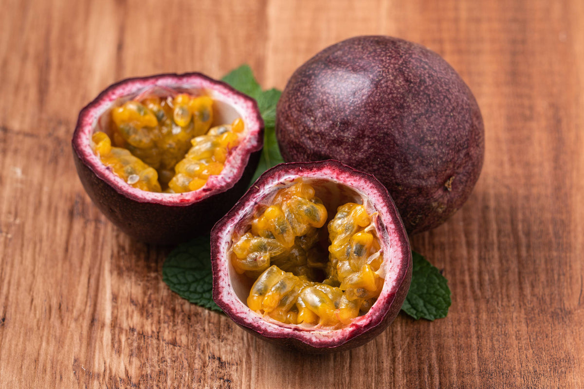 Reife Passionsfrucht mit dunkelvioletter Haut, zwei Hälften mit gelbem Fruchtfleisch
