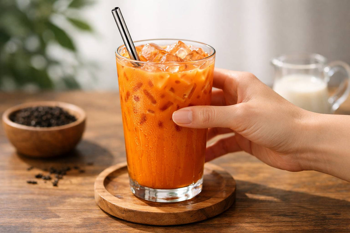 Ein Glas mit orangefarbenem Thai-Eistee, Eiswürfeln und Metallstrohhalm