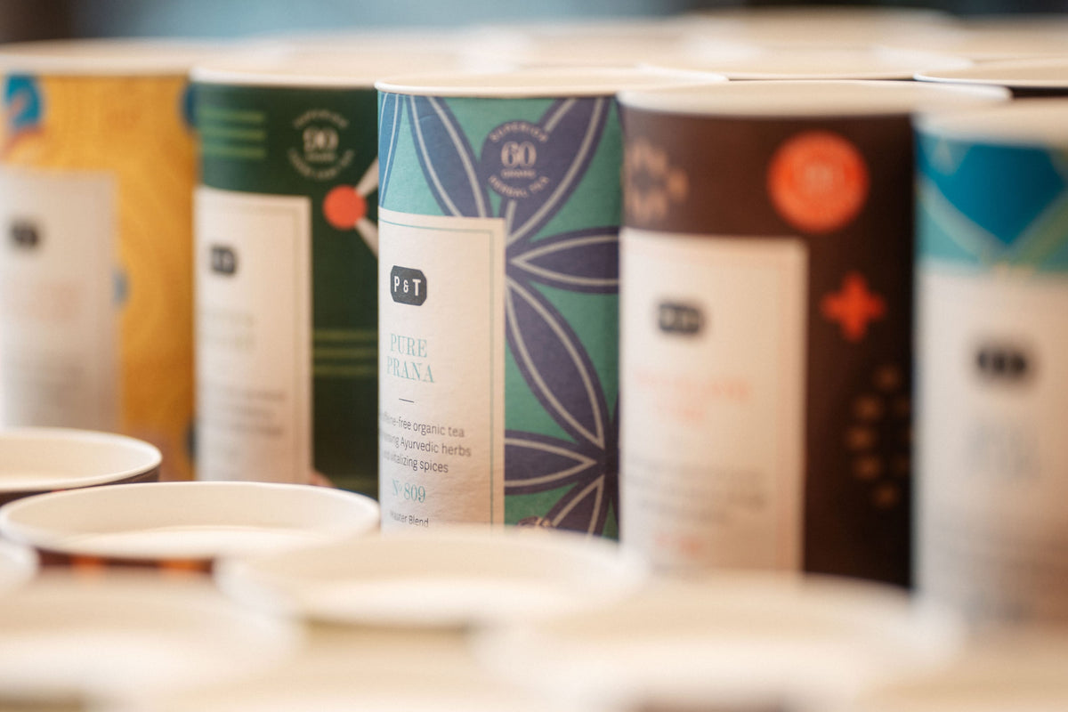 Nahaufnahme von mehreren zylindrischen Teedosen ‚Master Blends‘ von Paper & Tea mit bunten Designs und teils unscharfen Beschriftungen