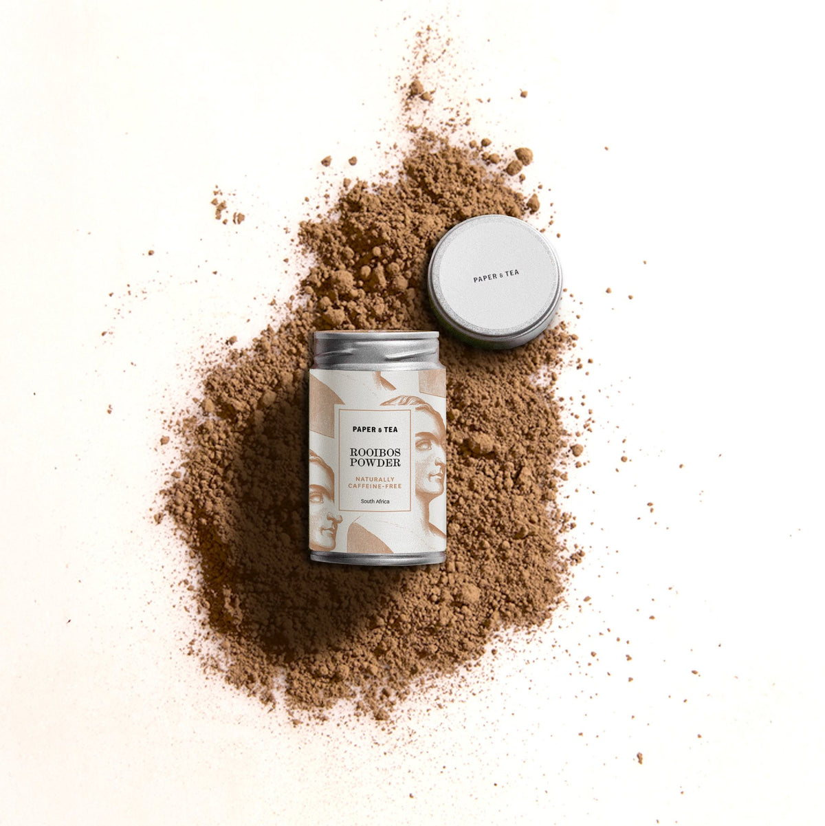 Elegante Dose mit Rooibos-Pulver von Paper & Tea, koffeinfrei, mit silbernem Deckel auf brauner Pulverschicht.