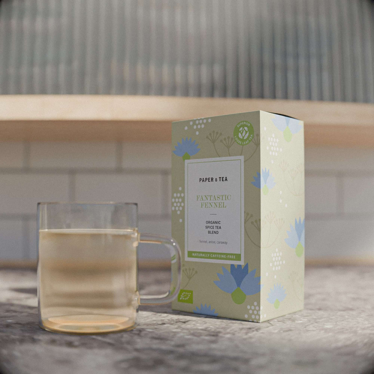 Beiger P&T Tee-Fantastic Fennel Karton und Glas mit hellbraunem Fencheltee auf Küchenarbeitsplatte.