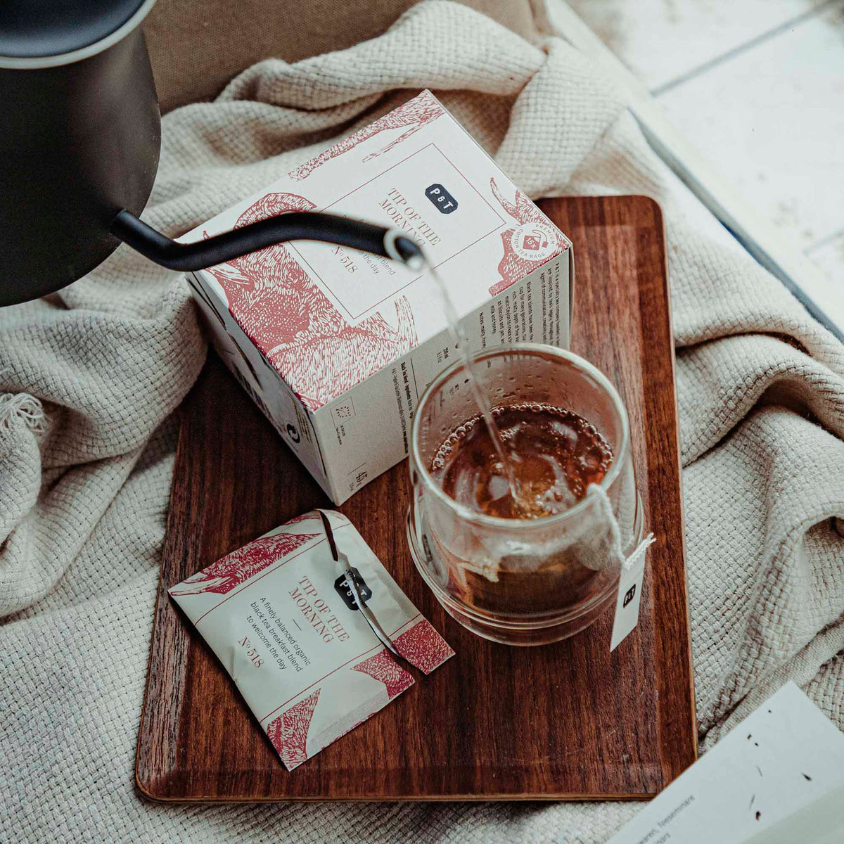Holztablett mit Bio-Schwarztee "TIP OF THE MORNING," Tee wird aus Kanne in Glastasse gegossen.
