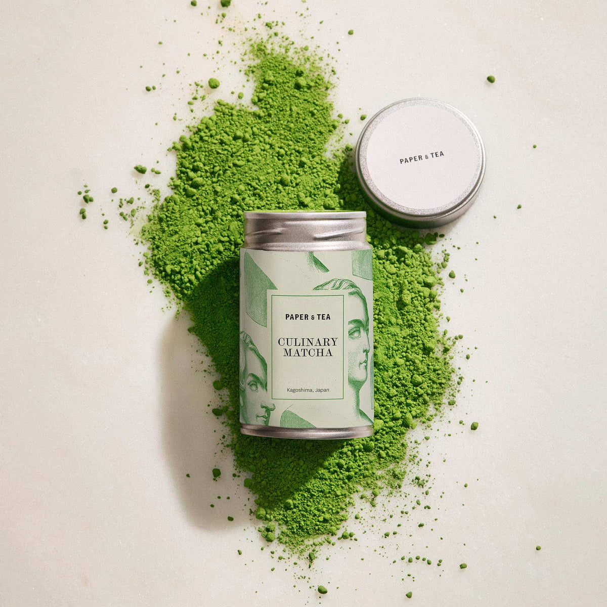 Silberne Dose mit künstlerischem Etikett für PAPER & TEA Culinary Matcha aus Kagoshima, umgeben von grünem Matcha-Pulver.