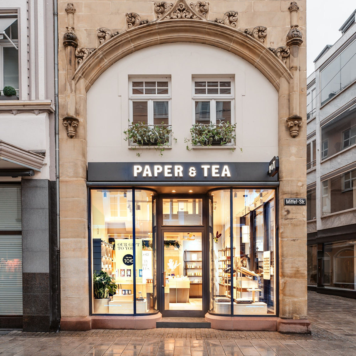 Eleganter PAPER & TEA Laden mit großen Glasfenstern und verziertem Sandsteinportal in der Mittelstraße.