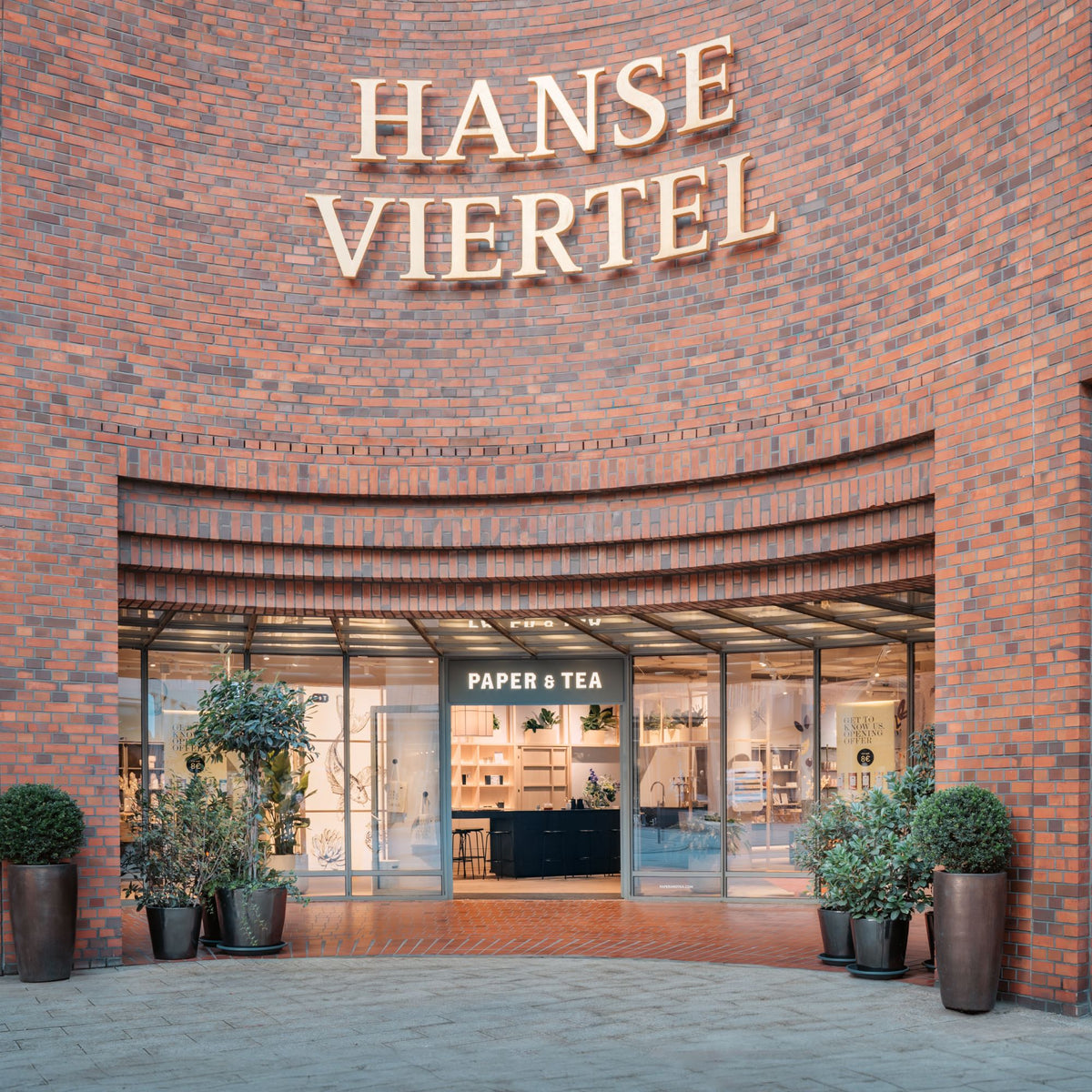 Eingang zu einem stilvollen Laden im Hanse Viertel, roter Backsteinbogen und PAPER & TEA Glasfront mit Pflanzen.