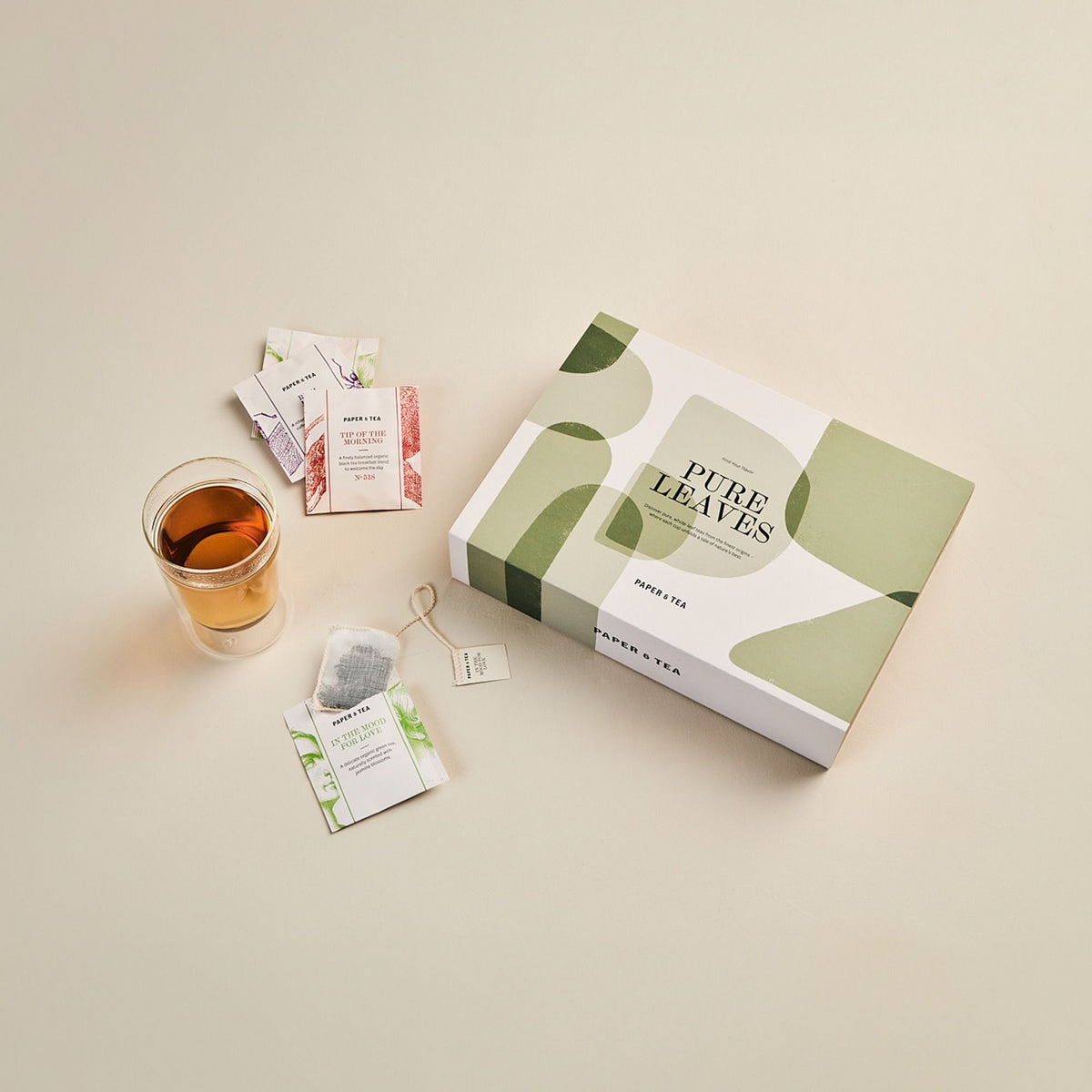 Elegante Tee-Komposition mit PURE LEAVES Box, Glas mit Tee und Bio-Teebeuteln Tip of the Morning & In the Mood for Love.