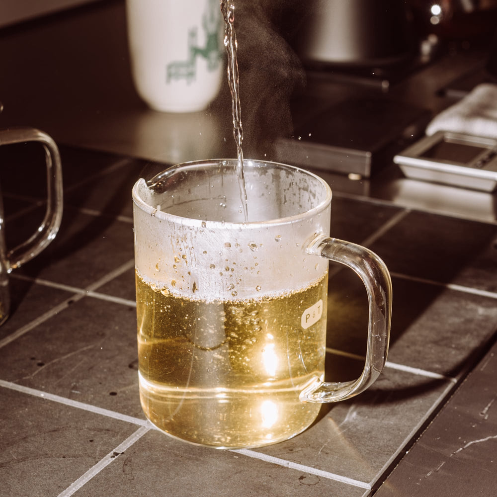 Glastasse mit dampfendem Tee und P & T Etikett auf gefliester Küchenarbeitsplatte.