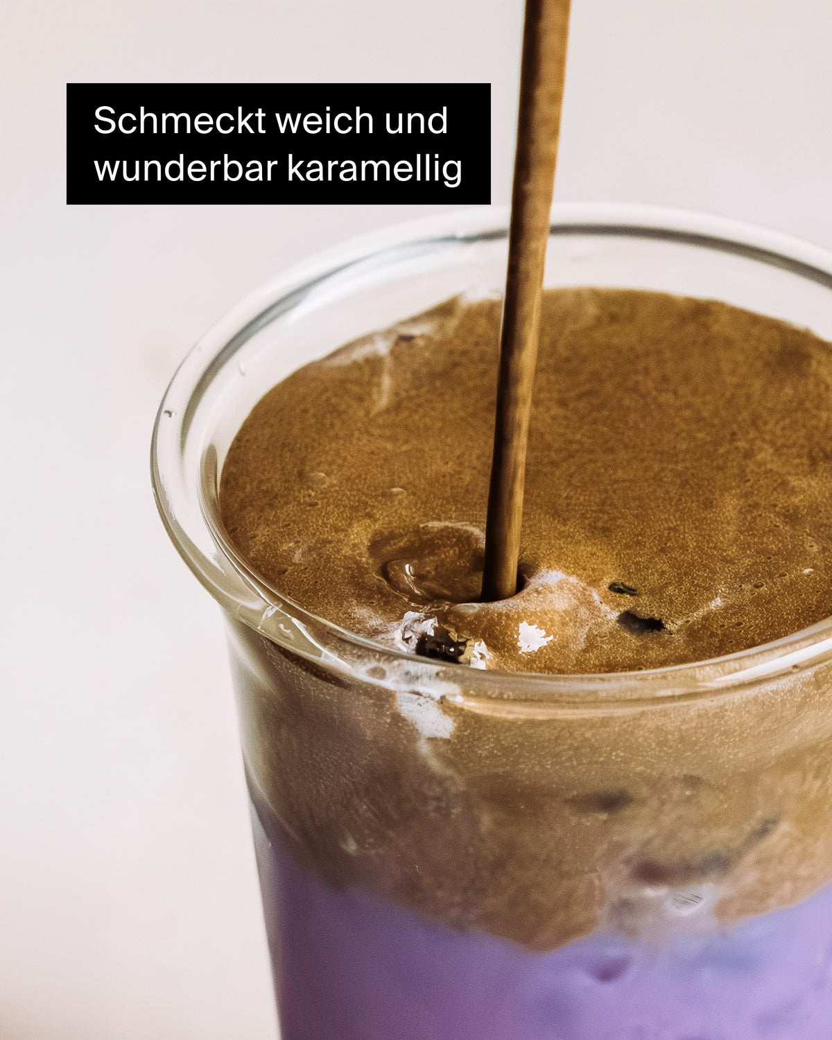 Glas mit geschichtetem Getränk, cremig hellvioletter Saft mit karamellfarbener Schaumkrone und Strohhalm