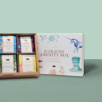 Offene 6GRACES Amenity Box mit sechs einzeln verpackten Produkten auf grünblauem Hintergrund