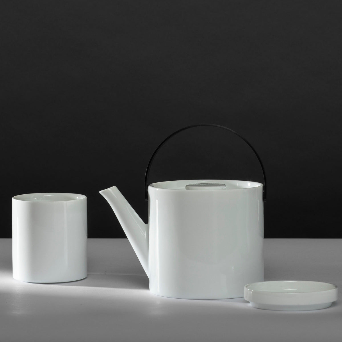 Modernes weißes Keramik-Teeservice mit Teekanne, Tasse und Untertasse auf grauem Hintergrund.