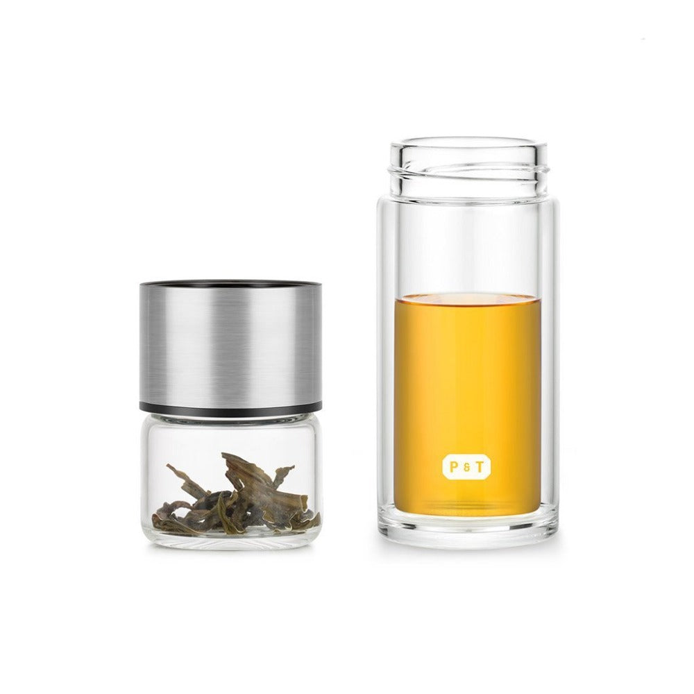 Doppelwandiges Glas mit bernsteinfarbenem Tee und Glasdose mit getrockneten Teeblättern, silberner Deckel