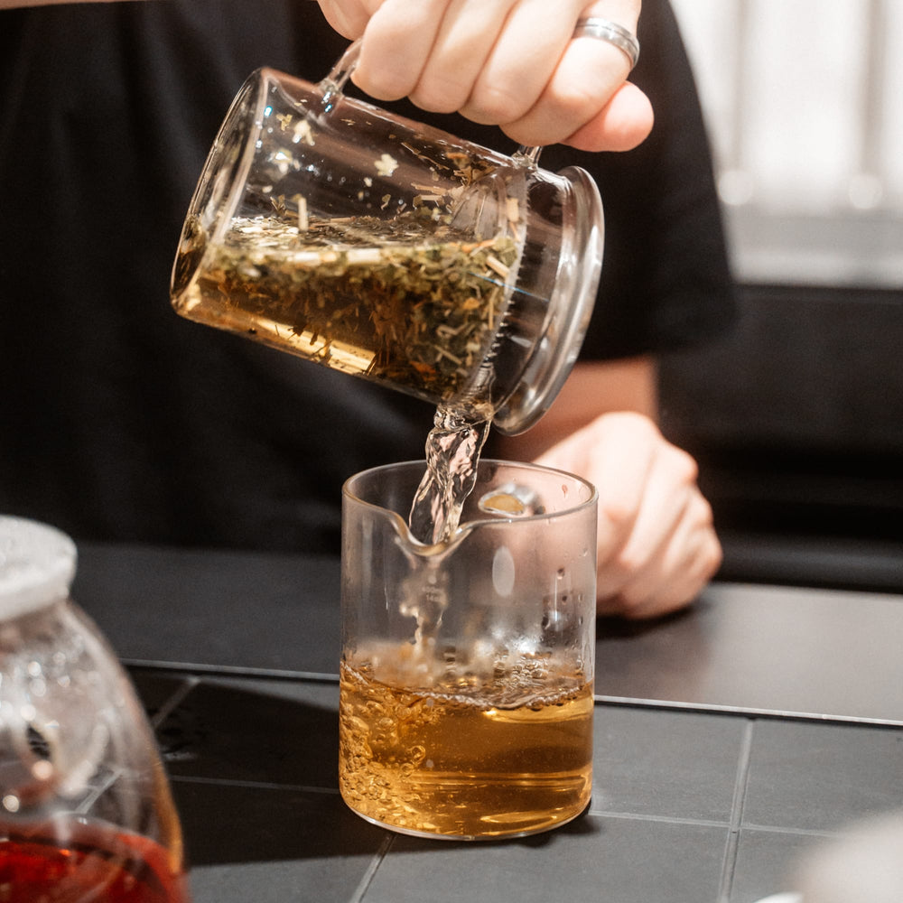 Brauner Tee aus Glas-Teebereiter in transparente Glastasse gegossen.